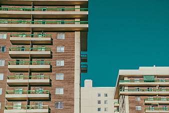Modern Brick Apartment Building with Green Railing Against Teal Sky