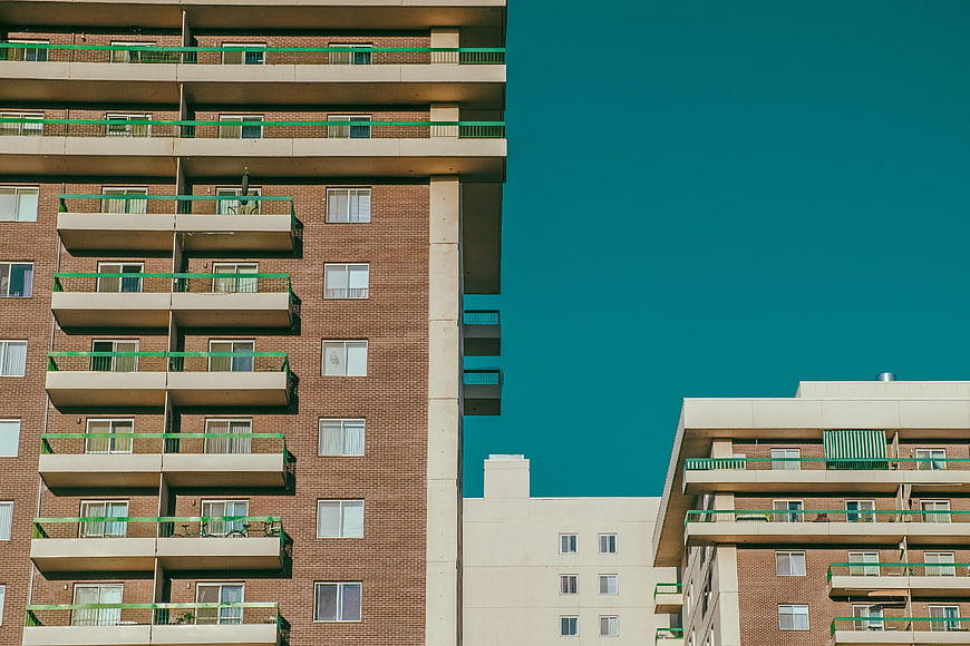 Modern Brick Apartment Building with Green Railing Against Teal Sky