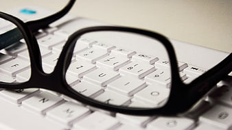 Black eyeglasses resting on a white computer keyboard close-up
