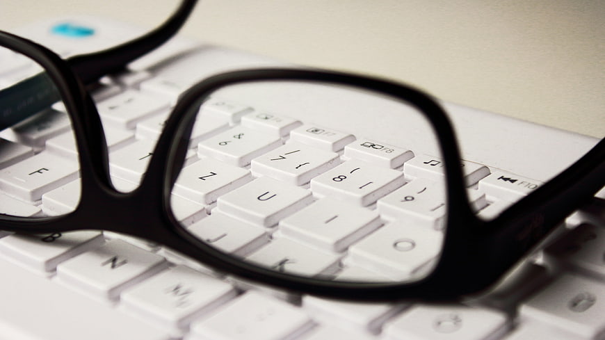 Black eyeglasses resting on a white computer keyboard close-up