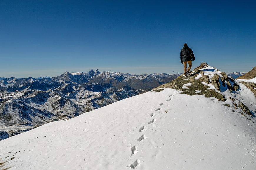 Hiker Standing on Snowy Mountain Summit with Panoramic Alpine View