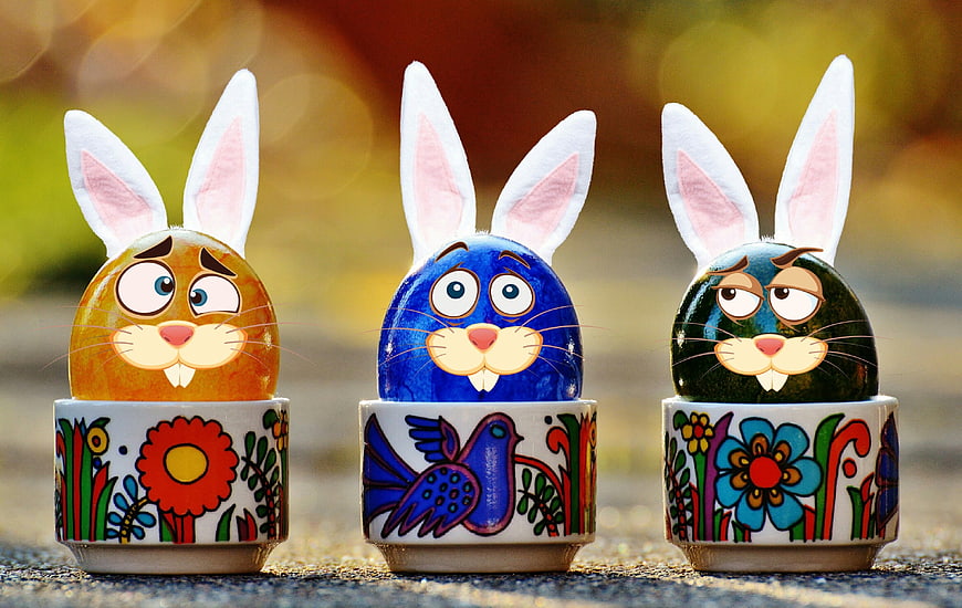 Three colorful Easter eggs with bunny ears in painted ceramic cups