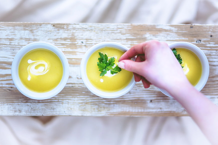 Overhead view of hand garnishing yellow soup with parsley