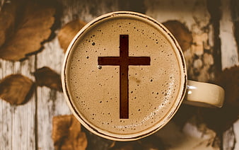 Top-down view of a coffee cup with a cross symbol on the foam