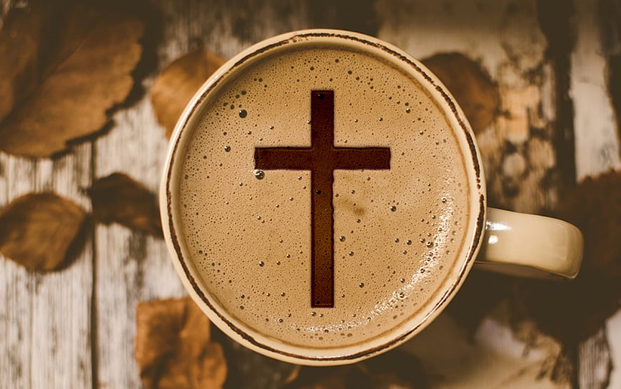 Top-down view of a coffee cup with a cross symbol on the foam