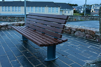 Wet Wooden Bench on Cobblestone Path in Rainy Town