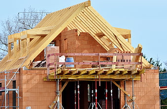 Wooden roof truss construction on brick house with scaffolding