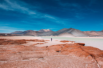 Lone Hiker Walking in Red Desert Landscape with Mountains