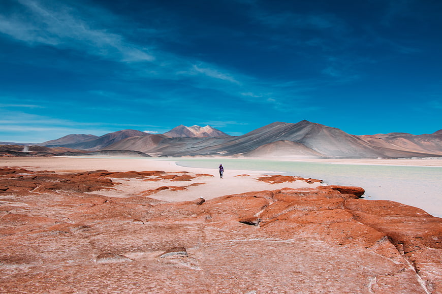 Lone Hiker Walking in Red Desert Landscape with Mountains