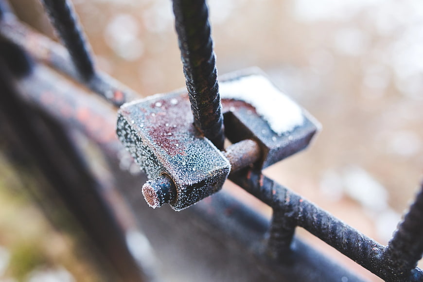 Rusty padlock covered in hoarfrost on metal gate