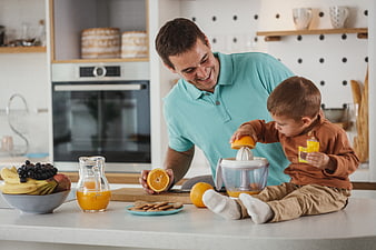 Happy father and son making fresh orange juice in kitchen