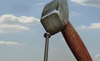 Close-up of hammer striking nail against blue sky