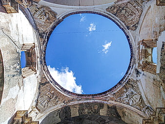 Circular opening in ruined cathedral looking up at blue sky