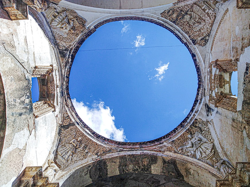 Circular opening in ruined cathedral looking up at blue sky