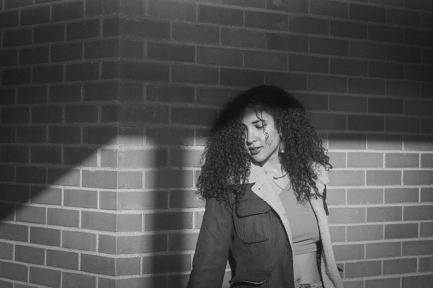 Black and white portrait of woman with curly hair against brick wall