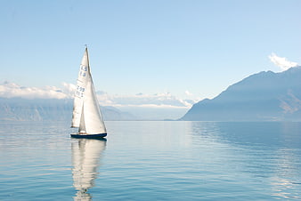 Lone Sailboat on Calm Lake with Mountain Background