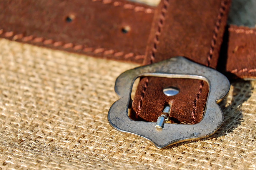 Close-up of vintage brown leather belt with metal buckle on burlap