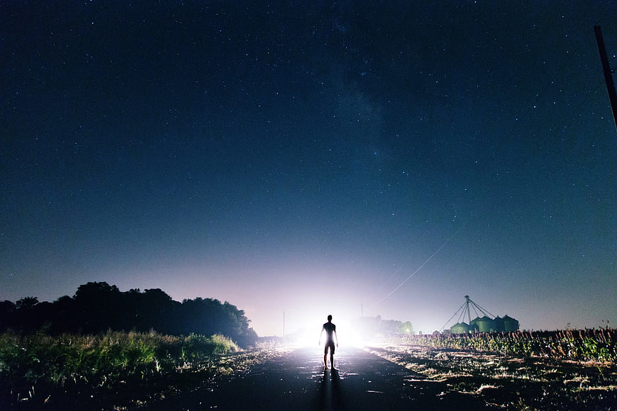 Silhouette of Man Walking on Rural Road Under Starry Night Sky