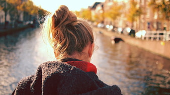 Woman with bun looking over canal in autumn city