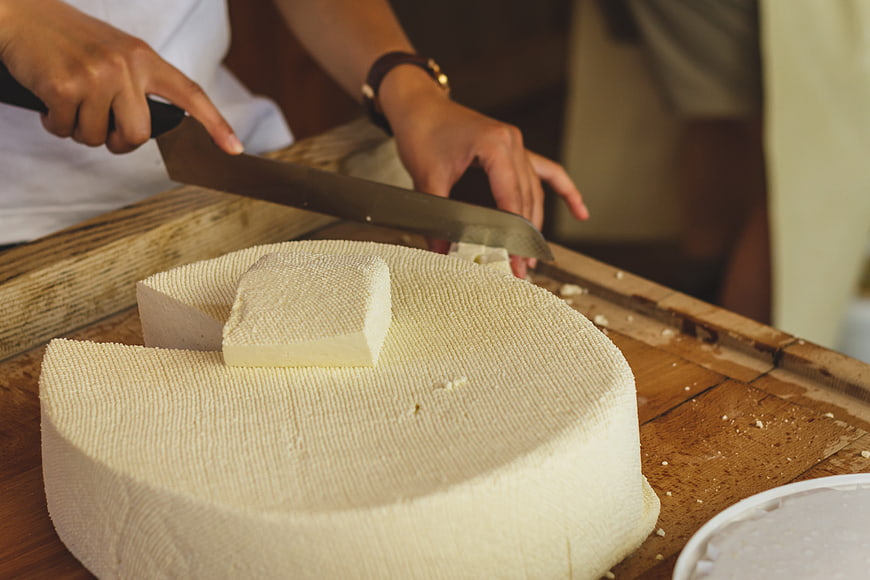 Artisan Cutting Fresh Alpine Cheese Wheel On Wooden Table