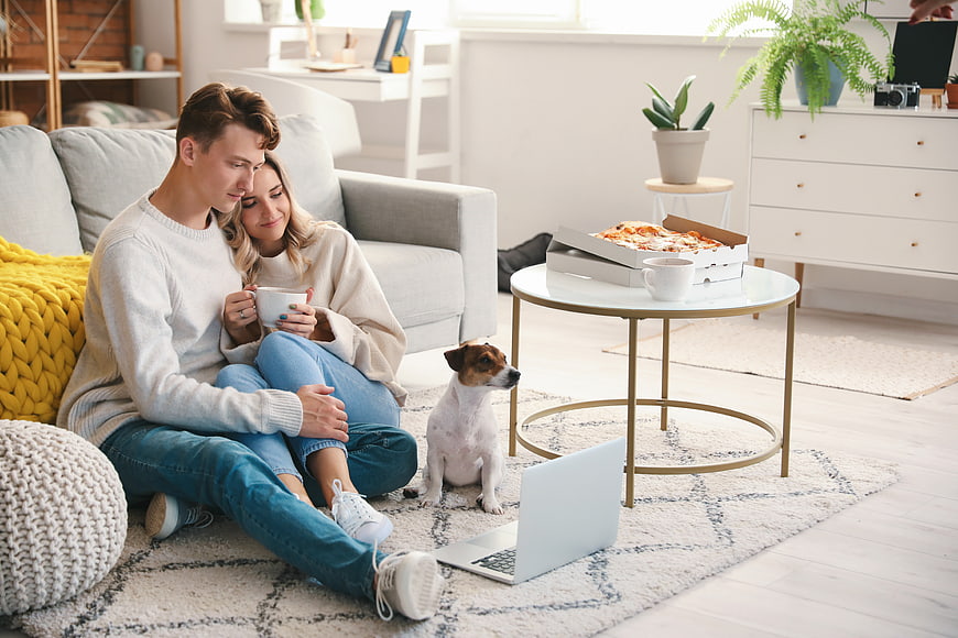 Young couple relaxing at home with dog and pizza