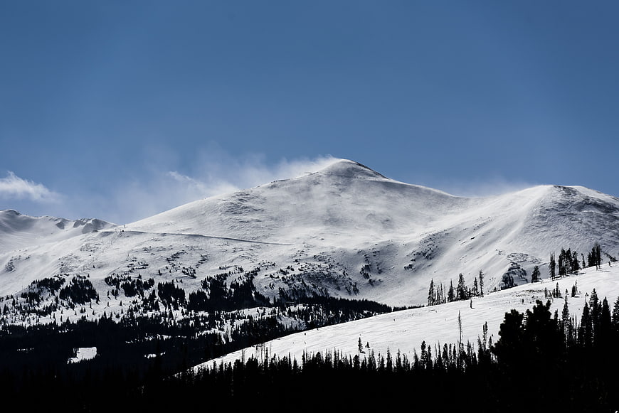 Snowy Mountain Peak with Blue Sky and Pine Forest