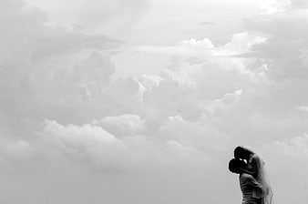 Black and white silhouette of a couple kissing under a cloudy sky