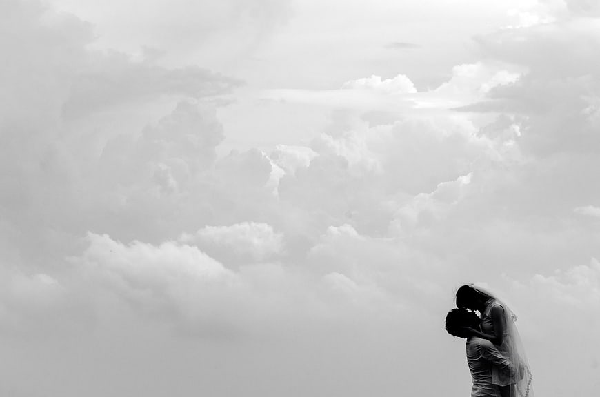 Black and white silhouette of a couple kissing under a cloudy sky