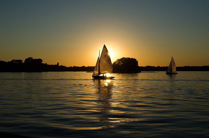 Silhouetted Sailboats on Calm Water at Golden Sunset