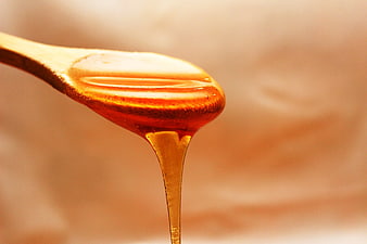 Golden Honey Dripping from Wooden Spoon Close Up