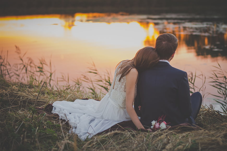 Wedding couple sitting by lake at sunset