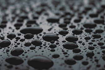 Close-up of dark water droplets on a textured surface