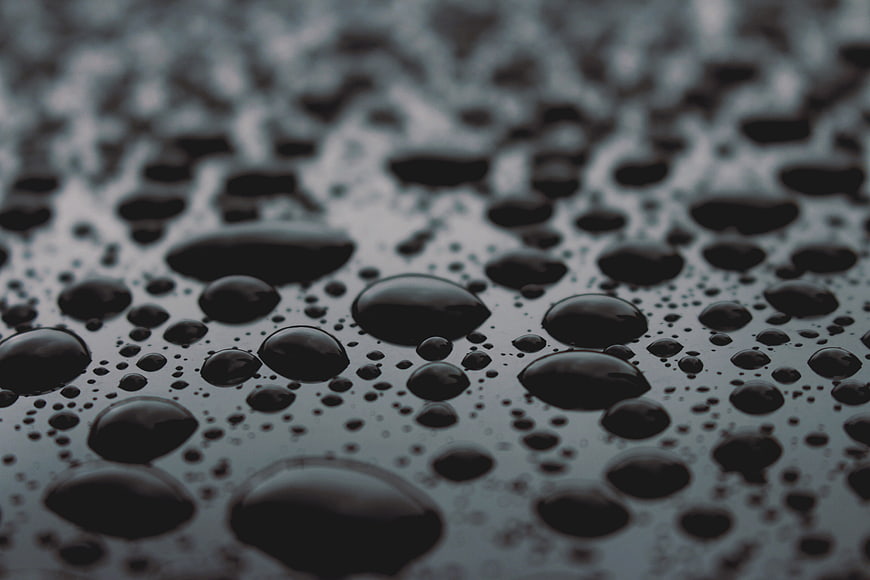 Close-up of dark water droplets on a textured surface