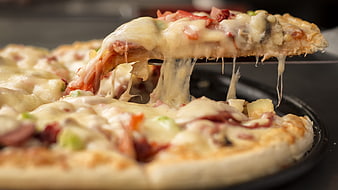 Close-up of cheesy pizza slice being lifted with toppings