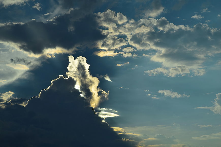 Dramatic Sun Rays Breaking Through Dark Clouds in Blue Sky