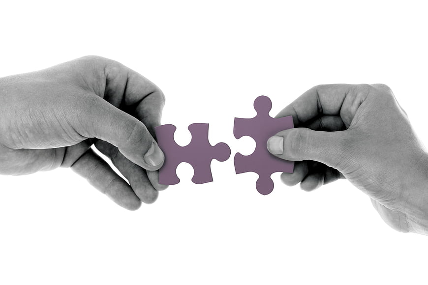Two Hands Connecting Purple Puzzle Pieces on White Background