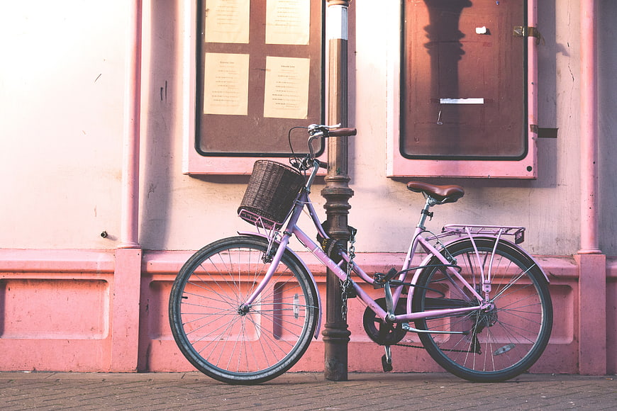 Pink Bicycle Leashed to Post Against Pink Wall