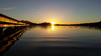 Sunset over calm lake with pier and mountain silhouette