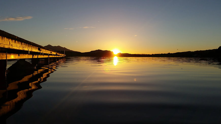 Sunset over calm lake with pier and mountain silhouette