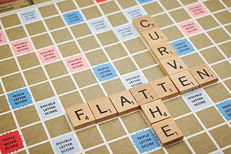 Scrabble tiles spelling flatten curve on game board