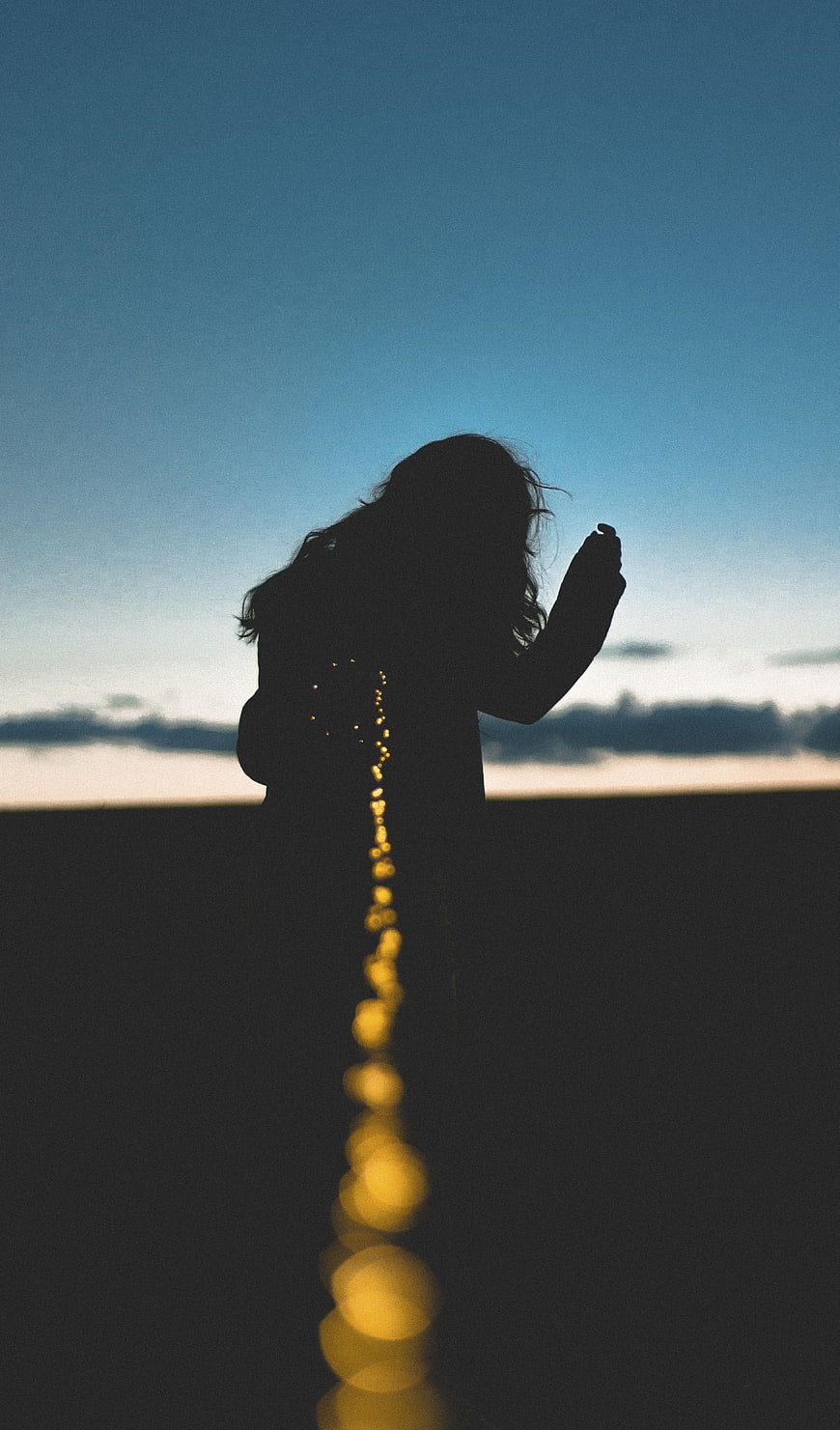 Silhouette of woman holding glowing lights against twilight sky