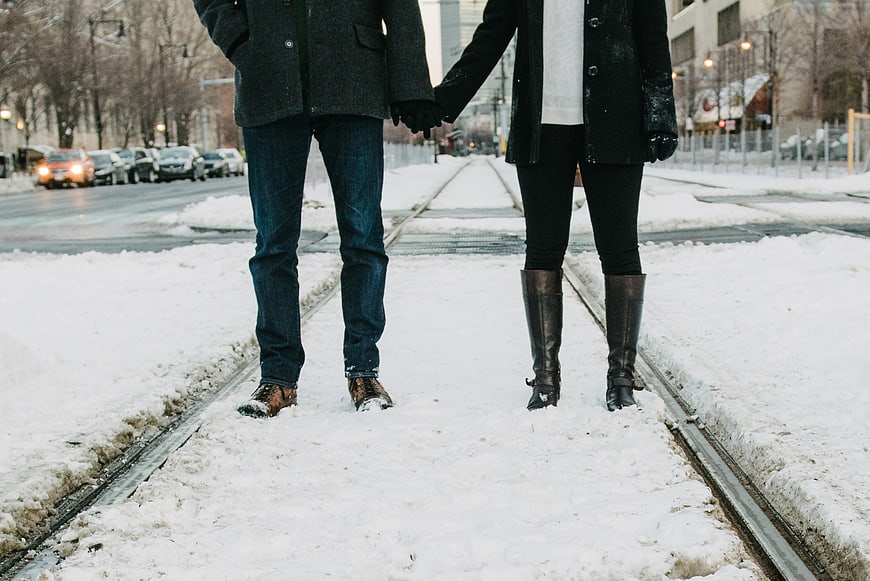 Couple Holding Hands Walking on Snowy Train Tracks