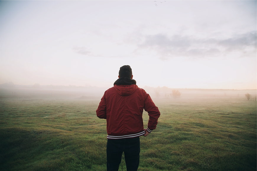Man in Red Jacket Standing in Foggy Field at Sunrise