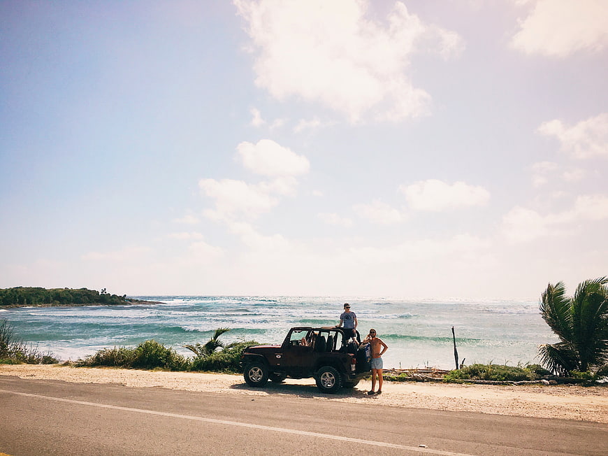 Jeep parked on coastal road with ocean view and travelers