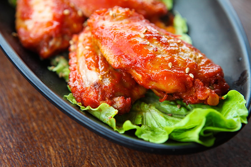 Glossy Red Glazed Chicken Wings On Black Plate With Lettuce
