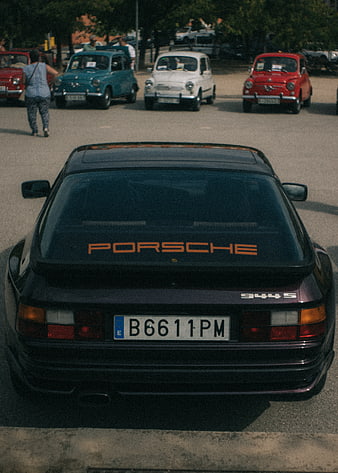 Rear view of classic black Porsche 944 S with vintage cars in background