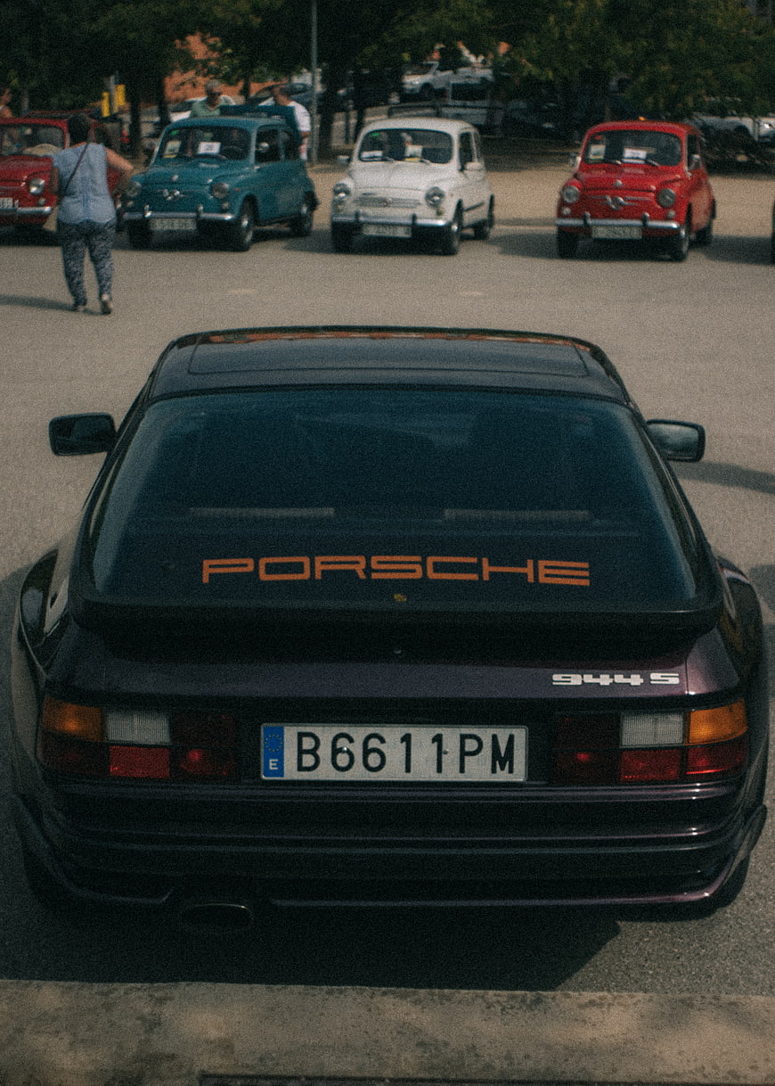 Rear view of classic black Porsche 944 S with vintage cars in background