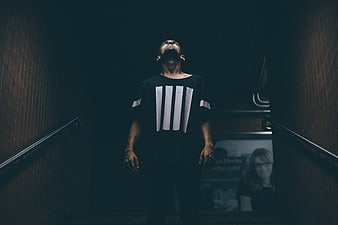 Man in Striped Shirt Looking Up on Dark Staircase