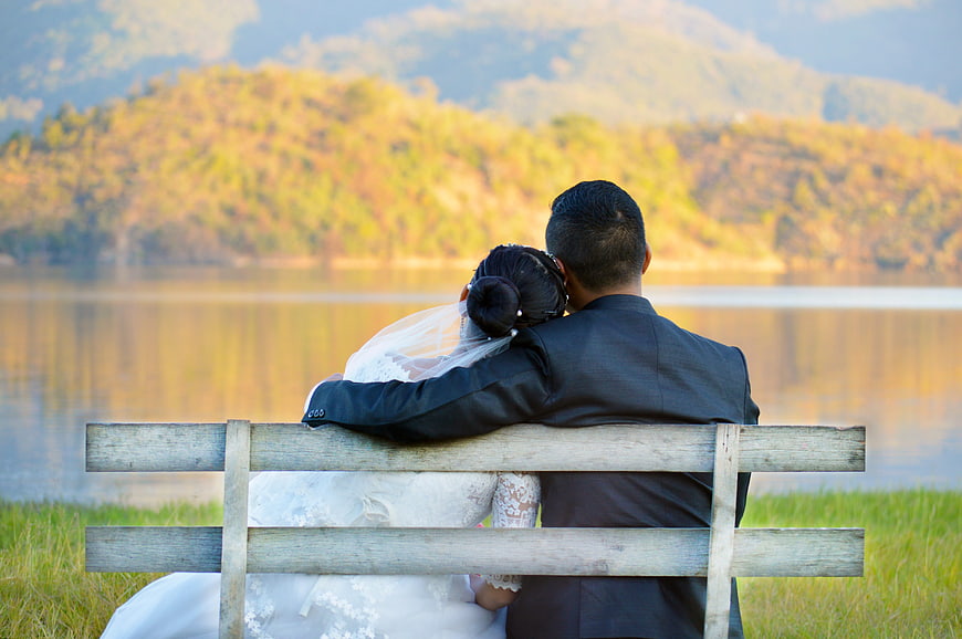 Romantic wedding couple sitting on a wooden bench by a lake