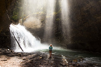 Woman standing in front of waterfall with sun rays